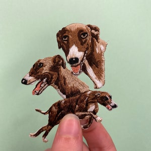 Puede incluir: Un parche bordado con un galgo de tres cabezas, en marrón y blanco.