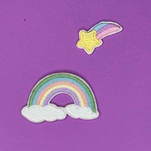May include: Two embroidered iron-on patches on a purple background. One patch is a rainbow with white clouds. The other patch is a yellow star with a rainbow tail.