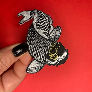 Könnte beinhalten: Schwarz-weiß gestickter Bügel-Patch mit einem Koi-Fisch mit gelben Akzenten. Der Fisch schwimmt nach rechts.