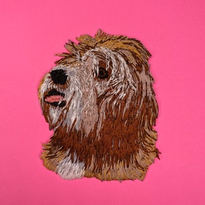 Peut inclure: Patch brodé représentant un chien brun et blanc avec la langue tirée, sur fond rose.