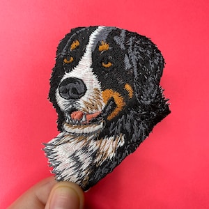 Può includere: Toppa ricamata con la testa di un cane da montagna bernese, con pelo nero, bianco e marrone. Il cane guarda a sinistra, con la lingua di fuori.