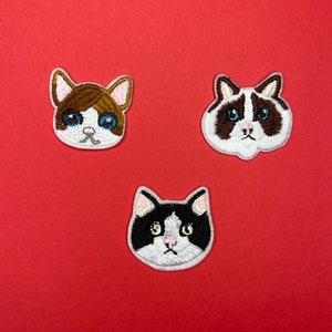 Puede incluir: Tres parches bordados para planchar con diferentes caras de gato. Los gatos tienen pelaje blanco con marcas marrones, negras y grises. Los gatos tienen ojos azules y narices rosas.