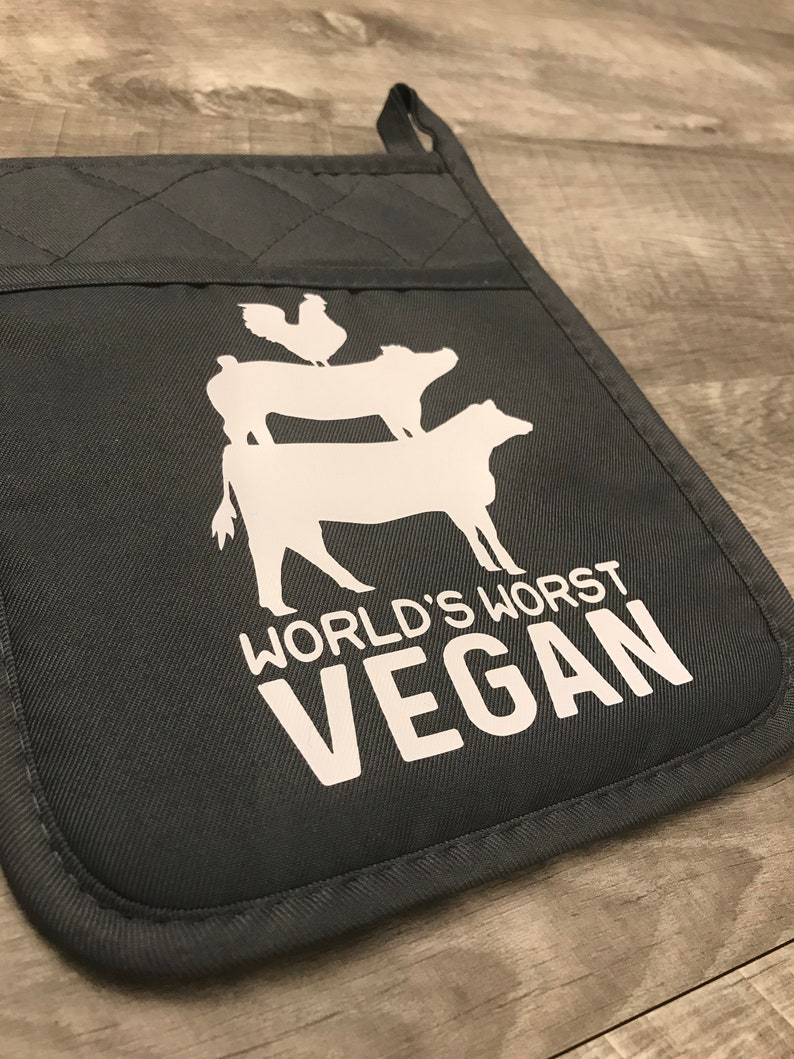 Peut inclure: Un gant de cuisine gris fonc&eacute; avec une silhouette blanche d'un poulet, d'un cochon et d'une vache empil&eacute;s les uns sur les autres. Le texte "WORLD'S WORST VEGAN" est imprim&eacute; en blanc sous les animaux.
