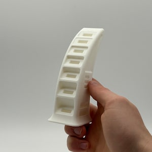 Könnte beinhalten: Weißer Magazinhalter aus Kunststoff mit 10 Fächern. Der Magazinhalter ist gebogen und hat einen flachen Boden.