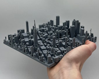 May include: A gray 3D printed model of a city skyline. The model is small enough to fit in the palm of a hand.