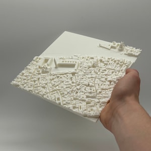 May include: A white 3D printed model of a city, possibly Venice, Italy. The model is detailed and shows the canals and buildings of the city.