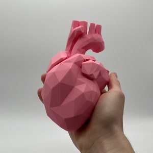 Op de afbeelding: Een roze, geometrisch gevormd hartbeeld. Het hart is gemaakt van veel kleine driehoeken en heeft een gedetailleerd, getextureerd oppervlak.