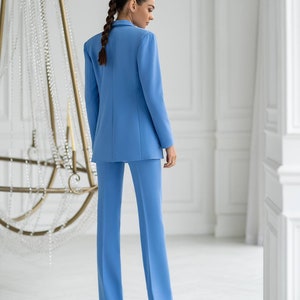 Puede incluir: Un traje de pantal&oacute;n azul claro con una chaqueta y pantalones de pierna recta. El traje est&aacute; hecho de una tela lisa y resistente a las arrugas.