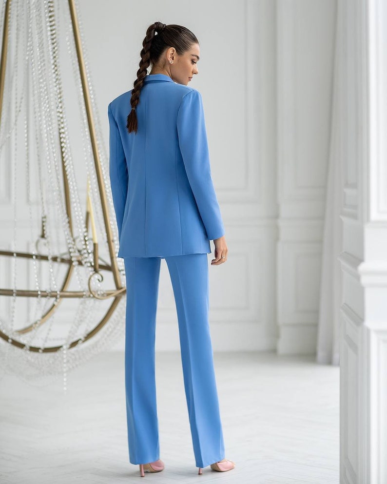 Puede incluir: Un traje de pantal&oacute;n azul claro con una chaqueta y pantalones de pierna recta. El traje est&aacute; hecho de una tela lisa y resistente a las arrugas.