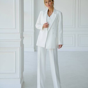 Puede incluir: Un traje de pantal&oacute;n blanco con una chaqueta de doble botonadura y pantalones de pierna ancha.