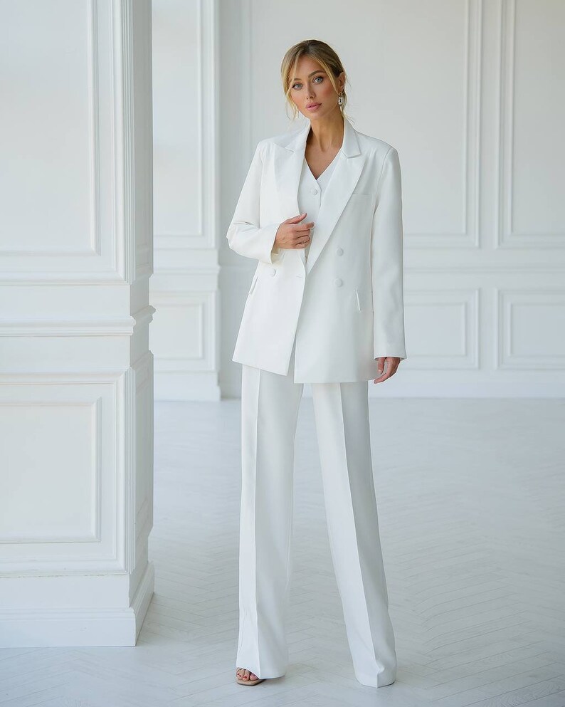 Puede incluir: Un traje de pantal&oacute;n blanco con una chaqueta de doble botonadura y pantalones de pierna ancha.