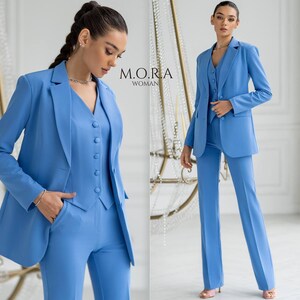Puede incluir: Dos mujeres con trajes azul claro a juego. El traje incluye una chaqueta, un chaleco y pantalones. El texto "M.O.R.A. WOMAN" es visible en la imagen.