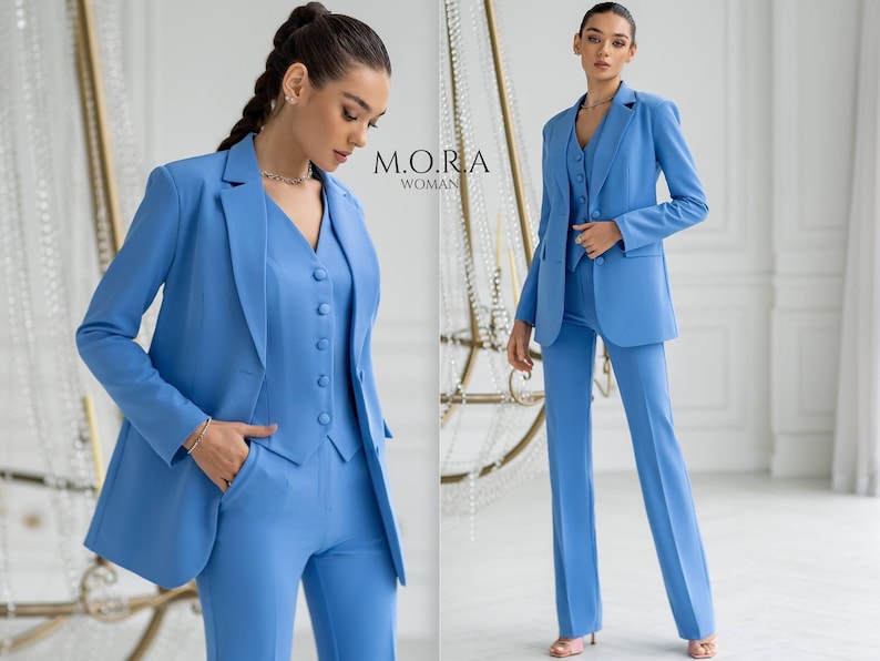 Puede incluir: Dos mujeres con trajes azul claro a juego. El traje incluye una chaqueta, un chaleco y pantalones. El texto "M.O.R.A. WOMAN" es visible en la imagen.