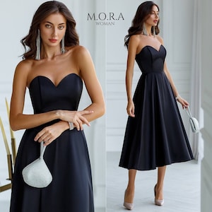 Puede incluir: Un vestido negro sin tirantes con escote de corazón y falda completa. El vestido es de largo hasta la rodilla y tiene un corpiño ajustado. La modelo lleva pendientes plateados y un bolso de mano plateado.