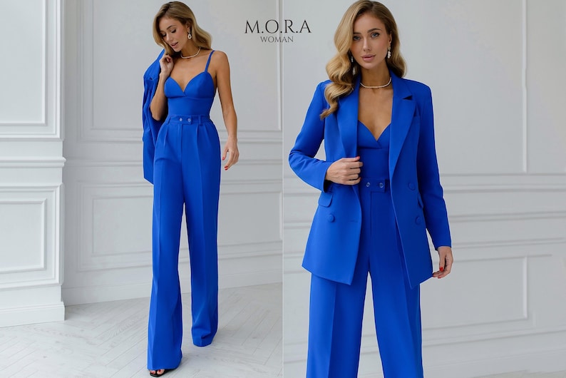 Pu&ograve; includere: Un completo pantalone blu reale con giacca e pantaloni a gamba larga. Il completo ha una parte superiore a V e una giacca doppiopetto. La modella indossa il completo con una collana.