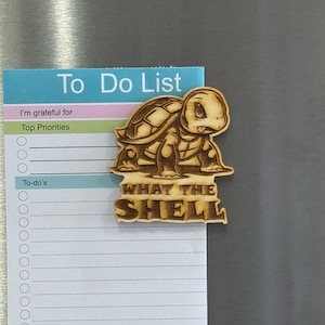 May include: A wooden turtle magnet with the text "What the Shell" on a white to-do list with the words "I'm grateful for" and "Top Priorities" at the top.