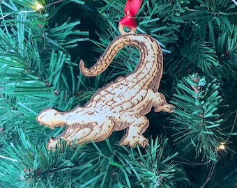 May include: A wooden alligator ornament with a red ribbon hanging from a Christmas tree.