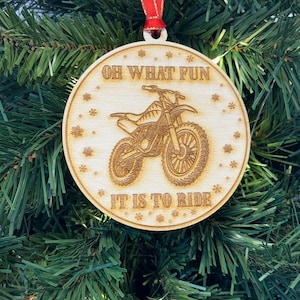 May include: A wooden Christmas bauble with a red ribbon. The bauble features a silhouette of a dirt bike with the text "Oh what fun it is to ride".