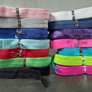 May include: A stack of colorful elastic bands in various colors, including pink, white, blue, purple, turquoise, green, black, and neon pink.
