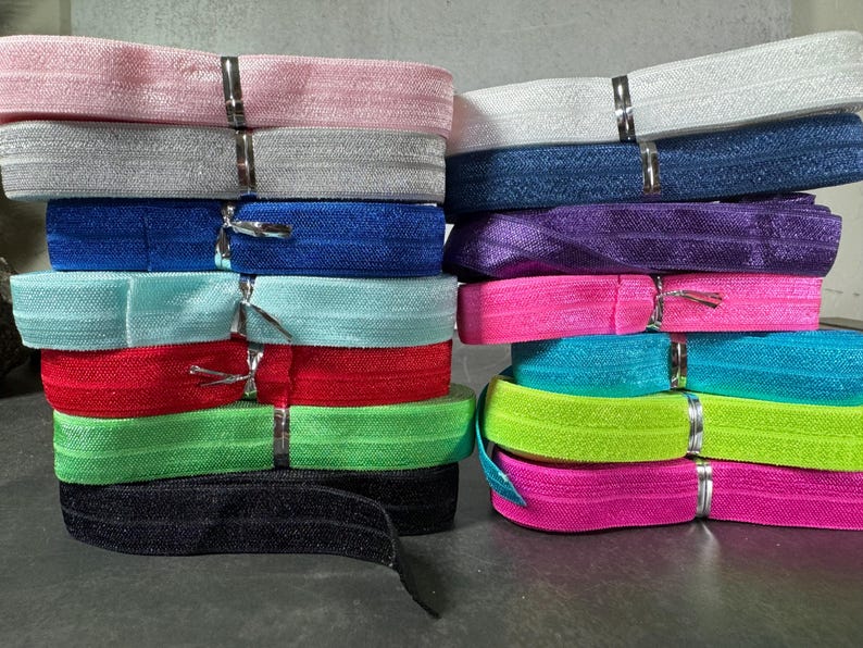 May include: A stack of colorful elastic bands in various colors, including pink, white, blue, purple, turquoise, green, black, and neon pink.