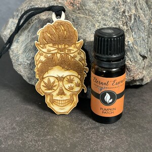 May include: Wooden cutout of a skull with a bandana and sunglasses, with a small bottle of essential oil labelled "Eternal Essence Premium Fragrance Oils Pumpkin Patch".