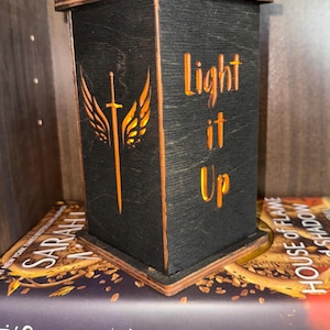Könnte beinhalten: Eine schwarze Holzlampe mit einem ausgeschnittenen Design eines Schwertes mit Flügeln und dem Text "Light it Up".
