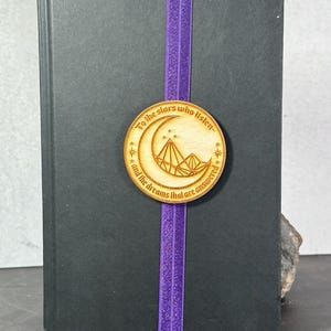 May include: A wooden bookmark with a crescent moon and mountain design. The bookmark has the text "To the stars who listen and the dreams that are answered".