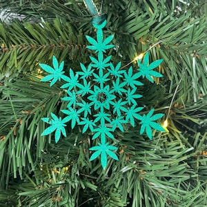 Puede incluir: Un adorno navideño verde con purpurina en forma de copo de nieve con diseños de hojas de marihuana.