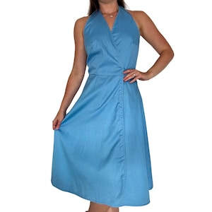 May include: A light blue halter dress with a V-neckline and a wrap-style bodice. The dress has a fitted waist and a flared skirt that falls to the mid-calf. The dress is made of a soft, lightweight fabric.