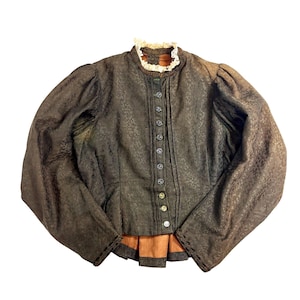 May include: A vintage brown jacket with a high collar and long sleeves. The jacket features a textured pattern, a row of buttons down the front, and a ruffled collar. The bottom of the jacket has an orange and brown trim.