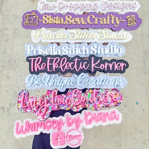 May include: A collection of colorful, layered acrylic business logo signs. The signs feature various names and designs, including "Sista Sew Crafty" with a sewing machine icon, and "Whimsey by Diana" with an Etsy logo.