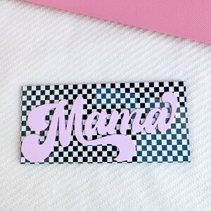 Pu&ograve; includere: Un cartello rosa "Mama" con uno sfondo a scacchi bianco e nero.