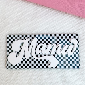 Pu&ograve; includere: Un cartello di legno bianco con la parola "Mama" in un font retr&ograve; su uno sfondo a scacchi bianco e nero.