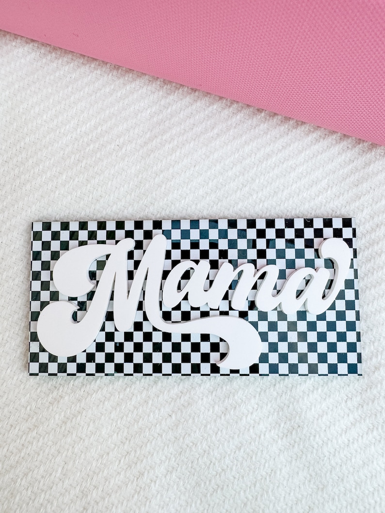 Pu&ograve; includere: Un cartello di legno bianco con la parola "Mama" in un font retr&ograve; su uno sfondo a scacchi bianco e nero.