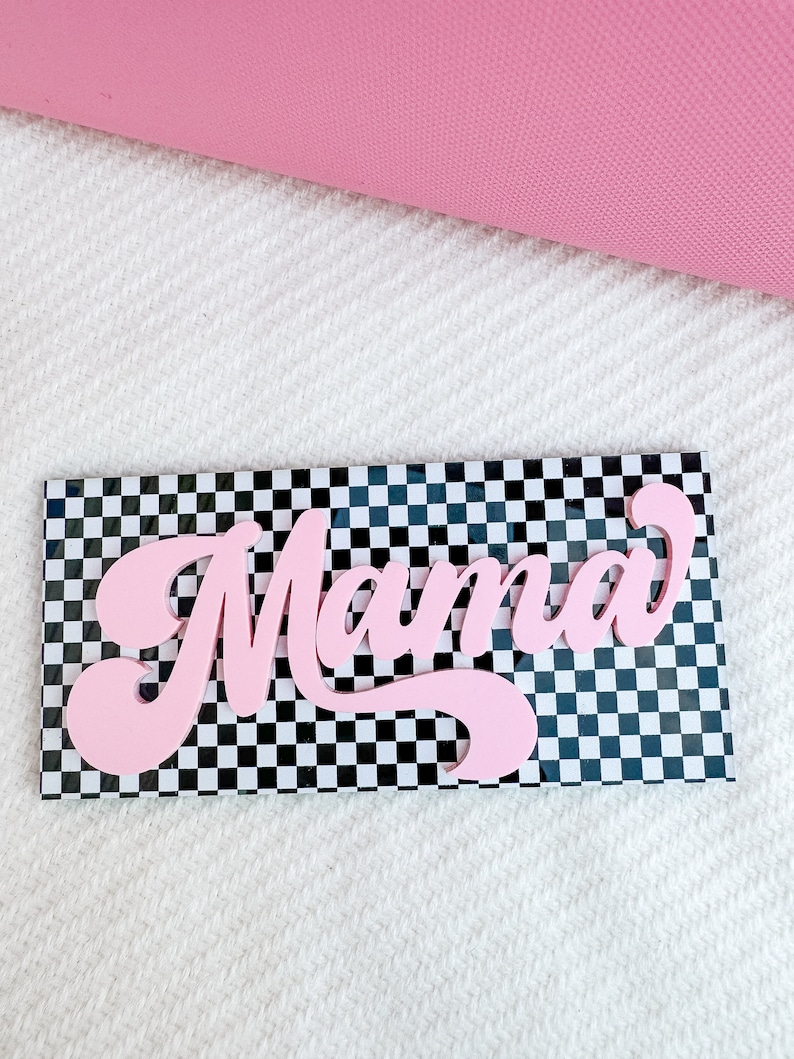Pu&ograve; includere: Un cartello rosa "Mama" con un font retr&ograve; su uno sfondo a scacchi bianco e nero.