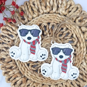 May include: Two white polar bear ornaments wearing sunglasses and red and gray scarves. The bears are sitting on a woven, circular placemat. Red flowers are in the upper left corner.