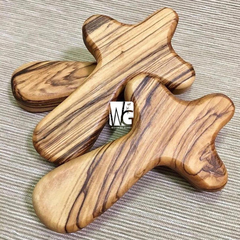 May include: Two wooden crosses made of olive wood. The crosses are intricately carved and have a natural wood finish. The crosses are stacked on top of each other.