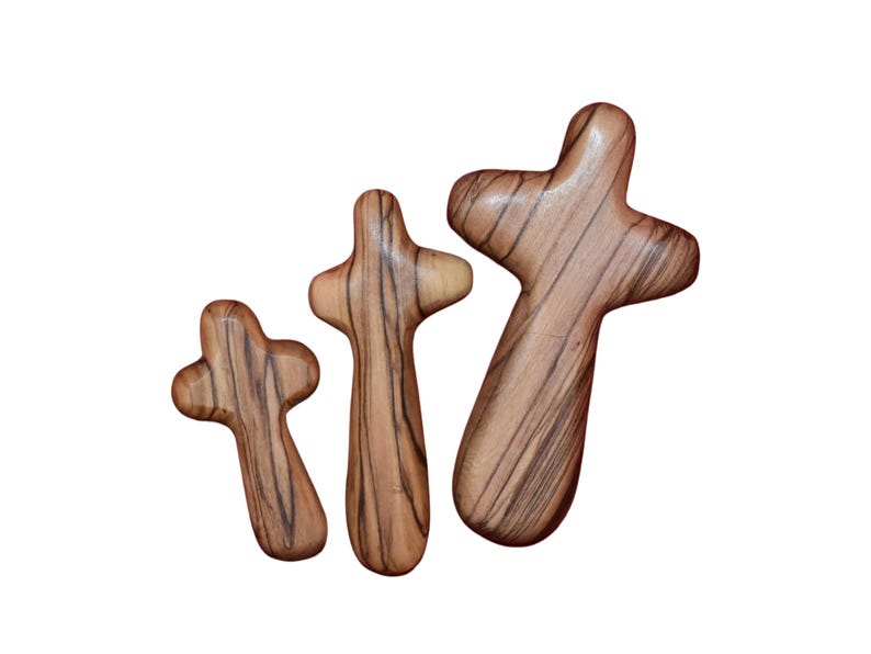 May include: Three wooden crosses of varying sizes, each with a natural wood grain pattern. The crosses are arranged in a row, with the largest cross on the right and the smallest cross on the left.