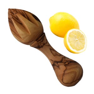 May include: A wooden lemon squeezer with a brown and olive wood grain pattern. The squeezer is shaped like a lemon and has a handle. Two lemons are in the background, one whole and one cut in half.