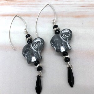 May include: A pair of silver dangle earrings featuring black and gray elephant charm beads and black teardrop beads.