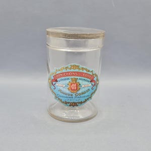 Puede incluir: Un tarro de vidrio transparente con una etiqueta azul y blanca que dice "Cornichons du Forez Vinaigre Forestier" y un escudo rojo con las letras "M.G."