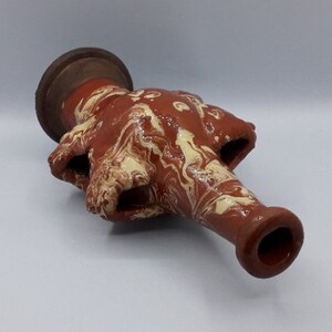 May include: A brown and cream ceramic vase with a marbled design. The vase has a wide base and a long, narrow neck.