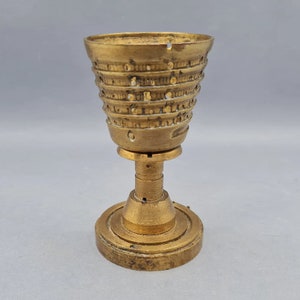 Op de afbeelding: Een gouden metalen eierdop met een decoratief, gepatroneerd ontwerp. De dop heeft een ronde basis en een hoge, cilindrische bovenkant.