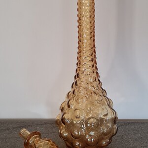 Pode incluir: Uma garrafa de vidro &acirc;mbar vintage com um design texturizado em forma de bolhas. A garrafa tem uma rolha combinando com uma ponta pontiaguda.