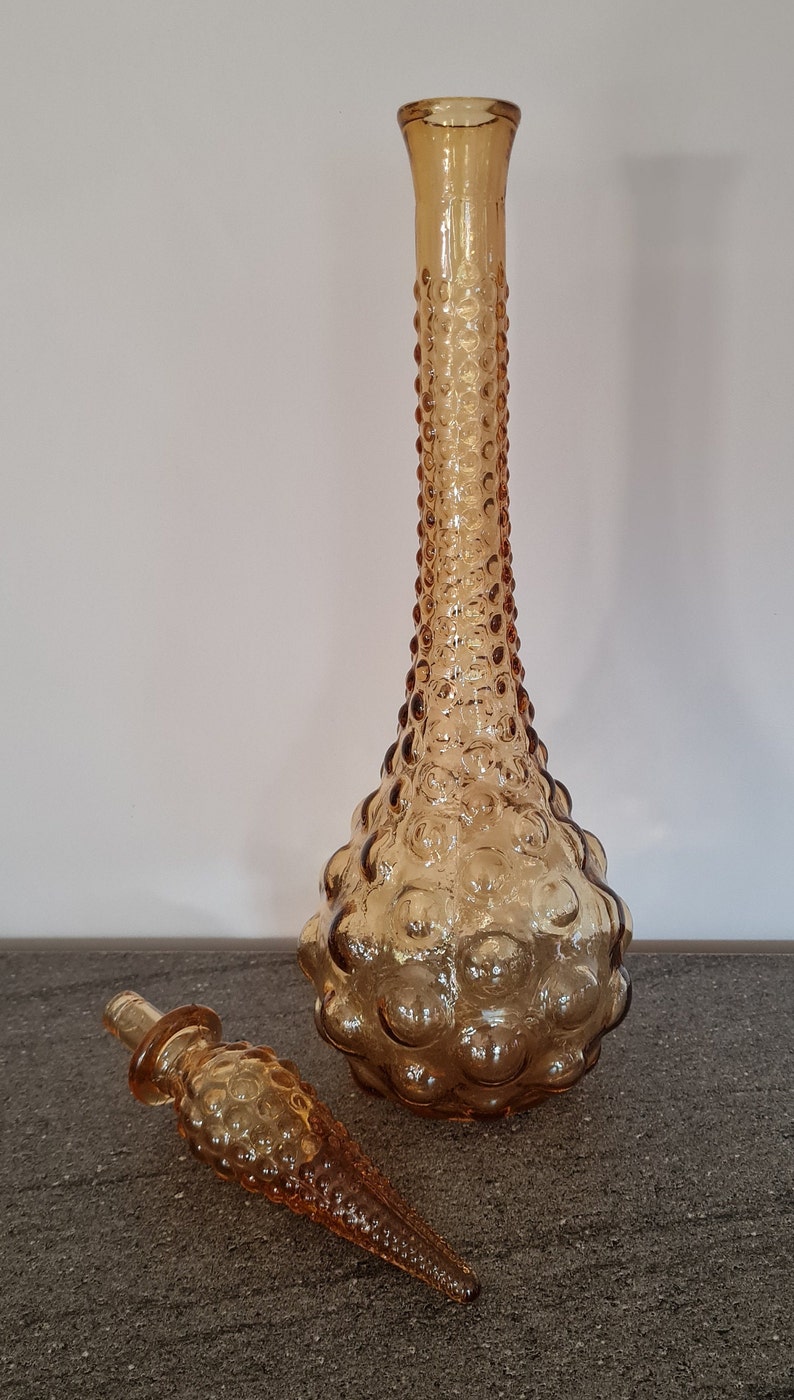 Pode incluir: Uma garrafa de vidro &acirc;mbar vintage com um design texturizado em forma de bolhas. A garrafa tem uma rolha combinando com uma ponta pontiaguda.