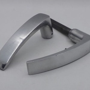 Może przedstawiać: Srebrny klamka do drzwi o zakrzywionym kształcie. Klamka jest wykonana z metalu i ma gładkie wykończenie.