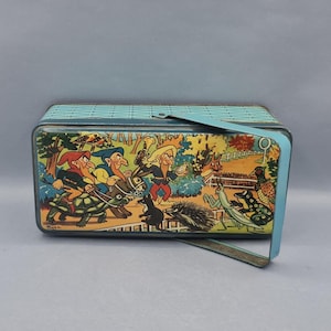 Puede incluir: Fiambrera metálica vintage con una escena de dibujos animados caprichosa. La fiambrera tiene un asa y un borde azul claro, con un patrón texturizado en la tapa. La obra de arte incluye una variedad de personajes y animales coloridos.