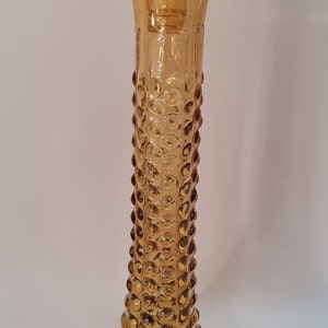 Pode incluir: Decantador de vidro &acirc;mbar com um design texturizado em forma de bolhas. O decantador tem um pesco&ccedil;o alto e fino e uma base larga e arredondada.
