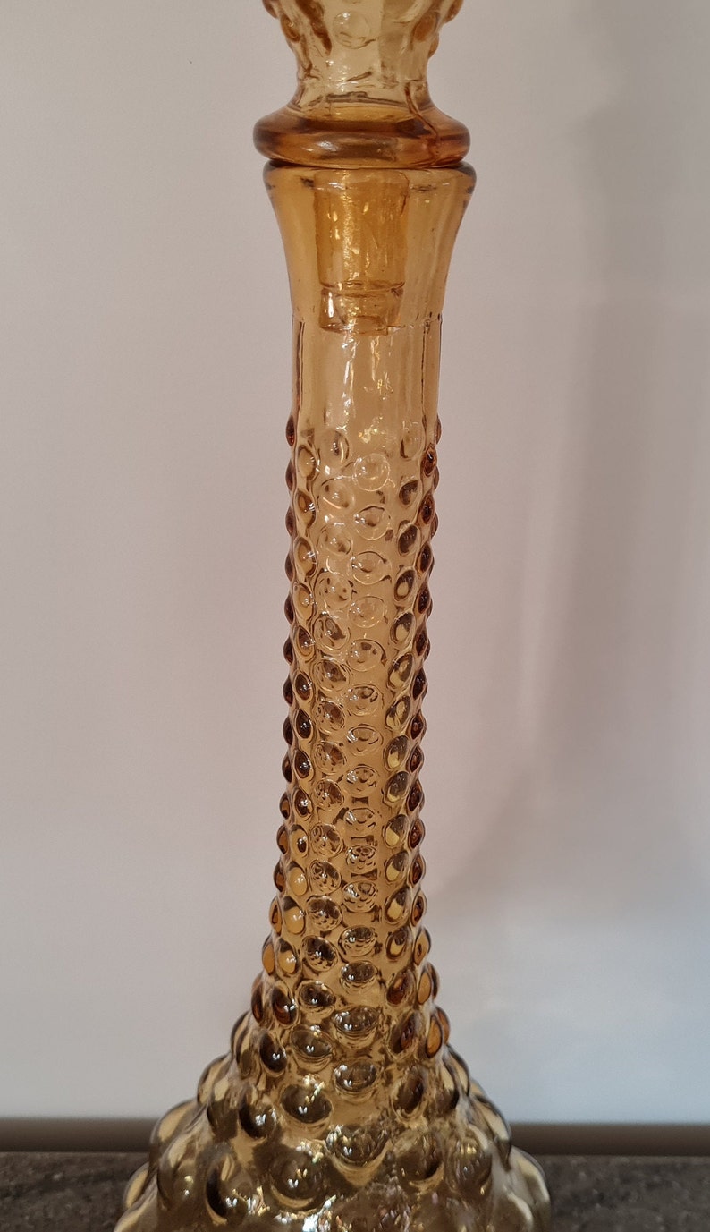 Pode incluir: Decantador de vidro &acirc;mbar com um design texturizado em forma de bolhas. O decantador tem um pesco&ccedil;o alto e fino e uma base larga e arredondada.