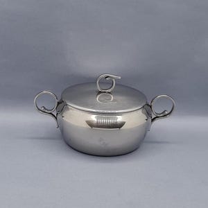 Peut inclure: Un sucrier en argent avec un couvercle et deux poignées. Le couvercle a une poignée en boucle décorative.